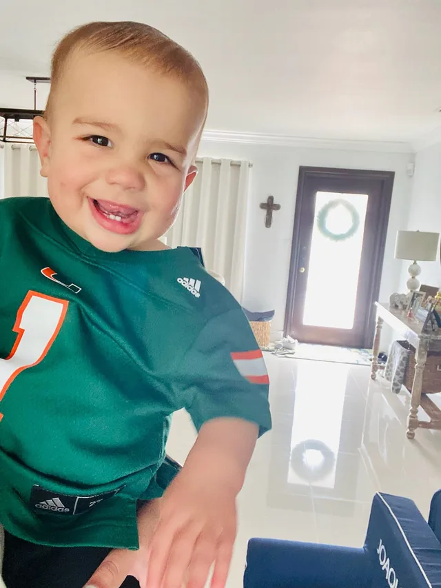 A young child wearing University of Miami Hurricanes fan gear with Eddie Gonzalez Loumiet